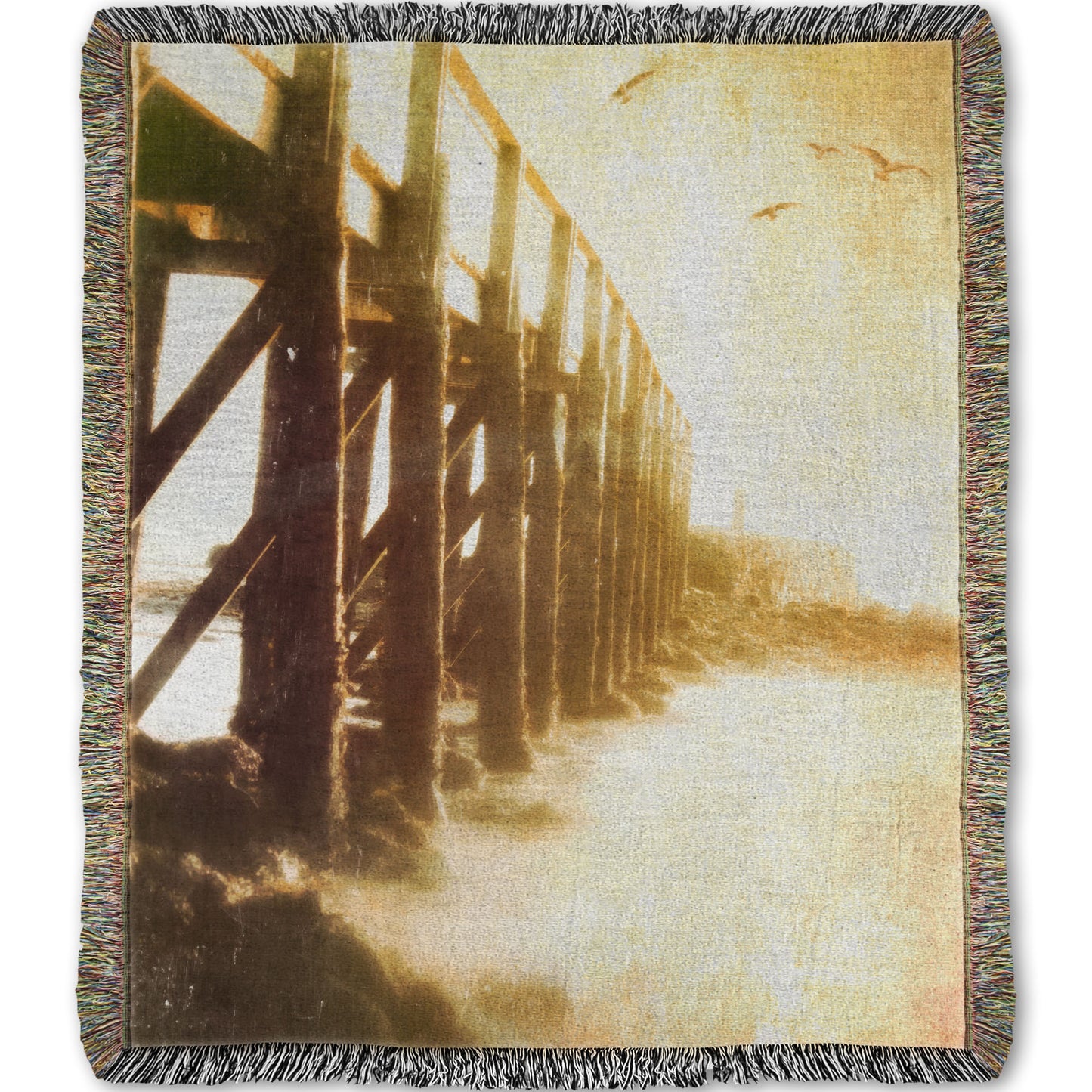 A woven throw blanket designed with a sepia photo looking out to sea along the side of a pier, as seagulls fly above.