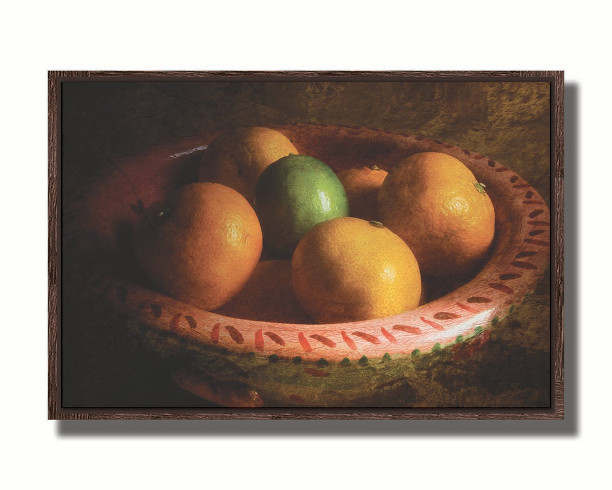 A photo of a bowl of oranges, with one lime placed in the center. Printed on canvas in a float frame.
