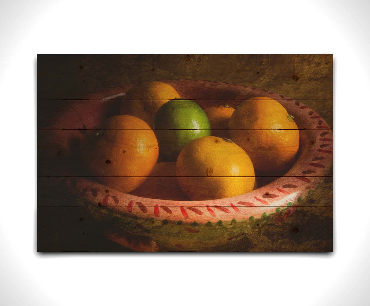 A photo of a bowl of oranges, with one lime placed in the center. Printed on a wood pallet.