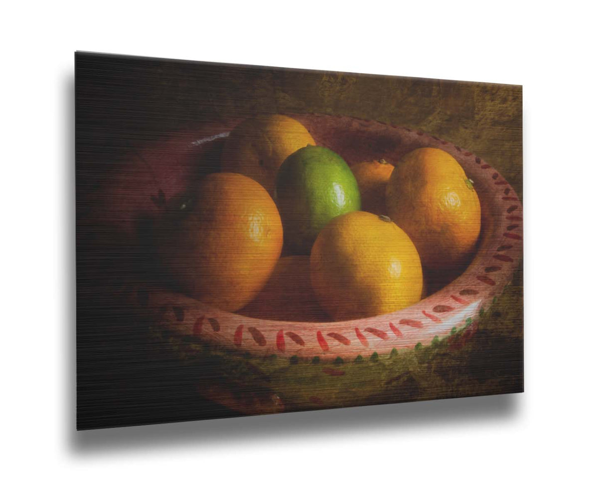A photo of a bowl of oranges, with one lime placed in the center. Printed on metal.