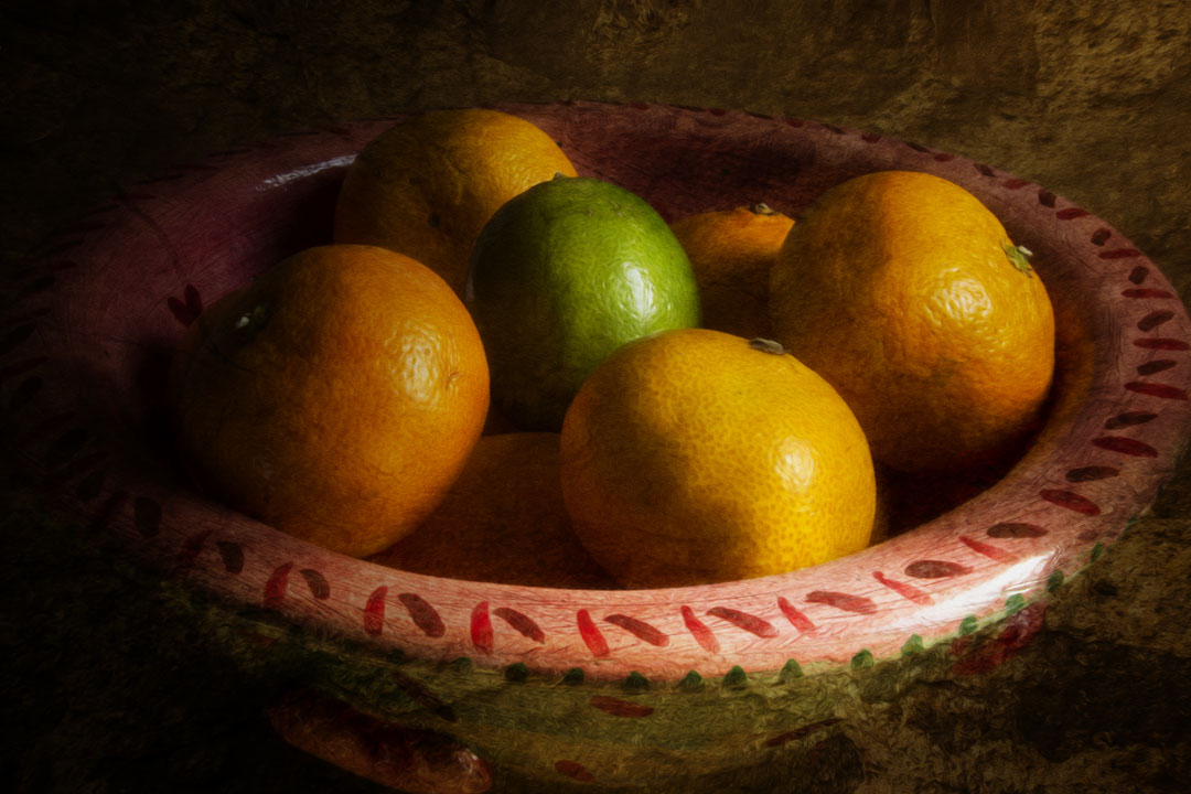A photo of a bowl of oranges, with one lime placed in the center.