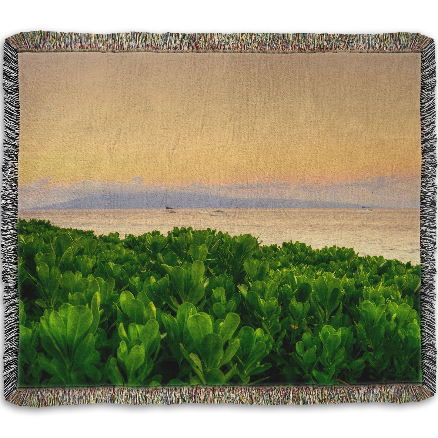 A woven throw blanket designed with a photo overlooking the sea from Kaanapali beach in Hawaii. Green plants fill the foreground, and boats sail on the water in the distance against a gentle orange sky and purple clouds.