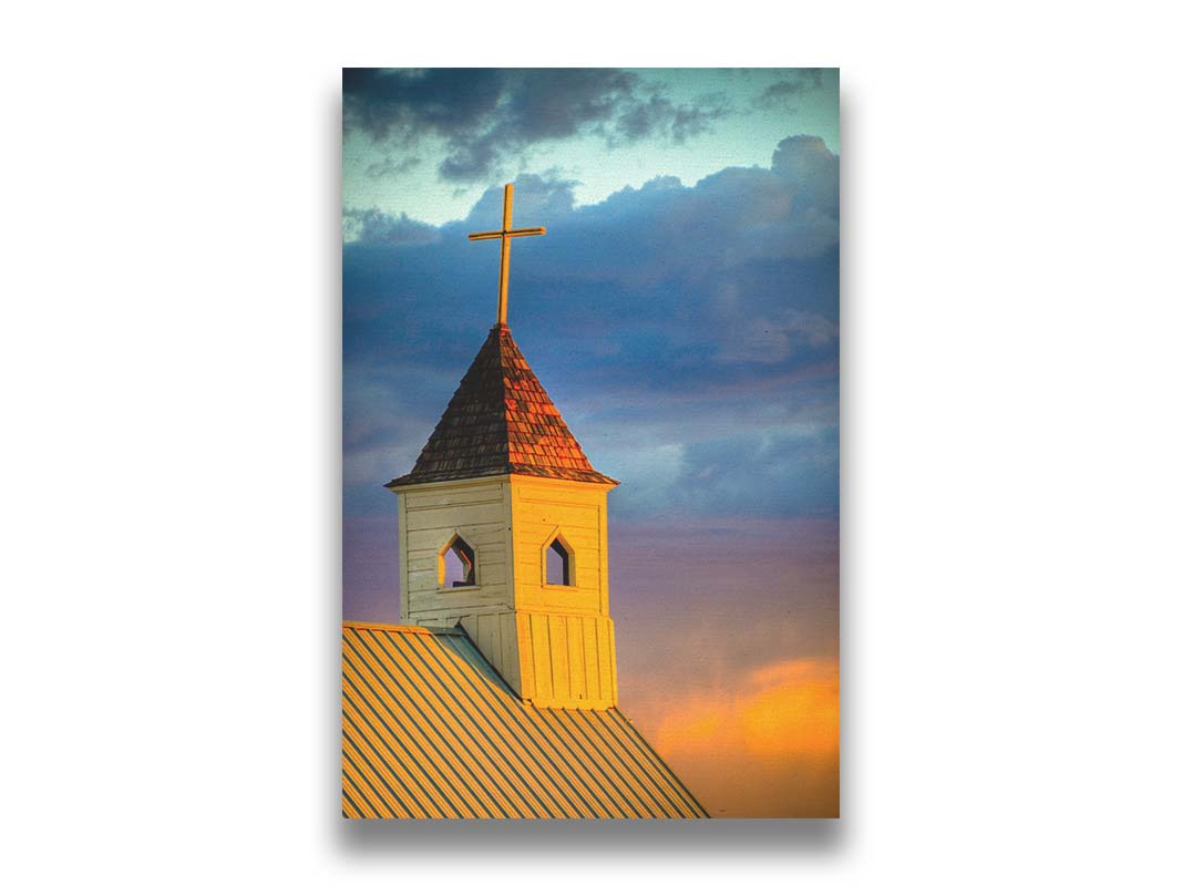 A photo of a cross-topped church at sunset, the sky gradating from blue to purple to orange. Printed on canvas.