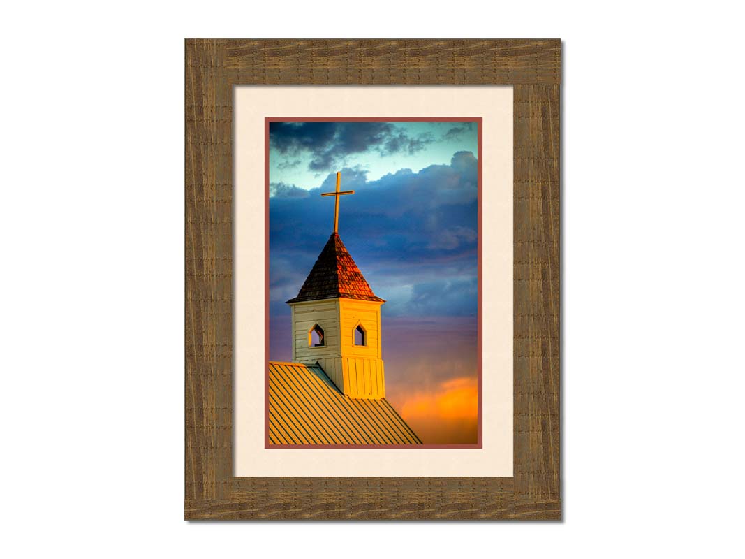 A photo of a cross-topped church at sunset, the sky gradating from blue to purple to orange. Printed on paper, matted, and framed.