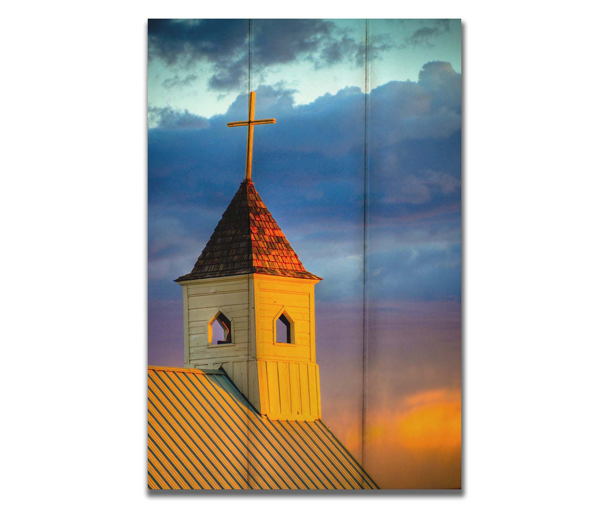 A photo of a cross-topped church at sunset, the sky gradating from blue to purple to orange. Printed on a box board.