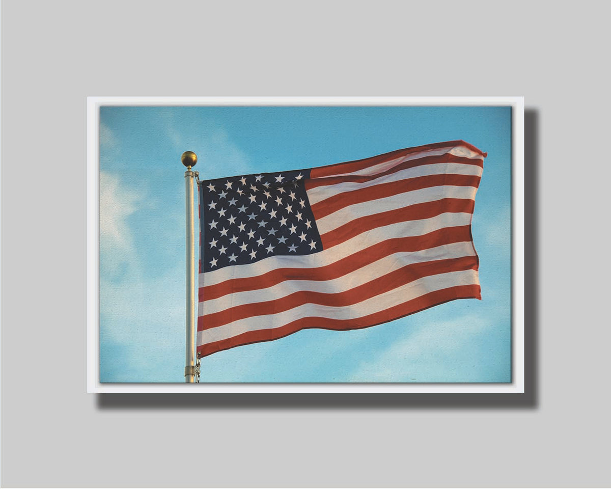 A photo of an American flag against a bright blue sky. Printed on canvas in a float frame.