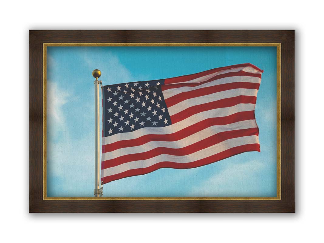 A photo of an American flag against a bright blue sky. Printed on canvas and framed.