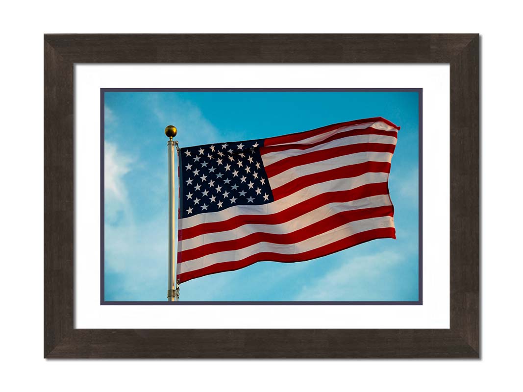A photo of an American flag against a bright blue sky. Printed on paper, matted, and framed.
