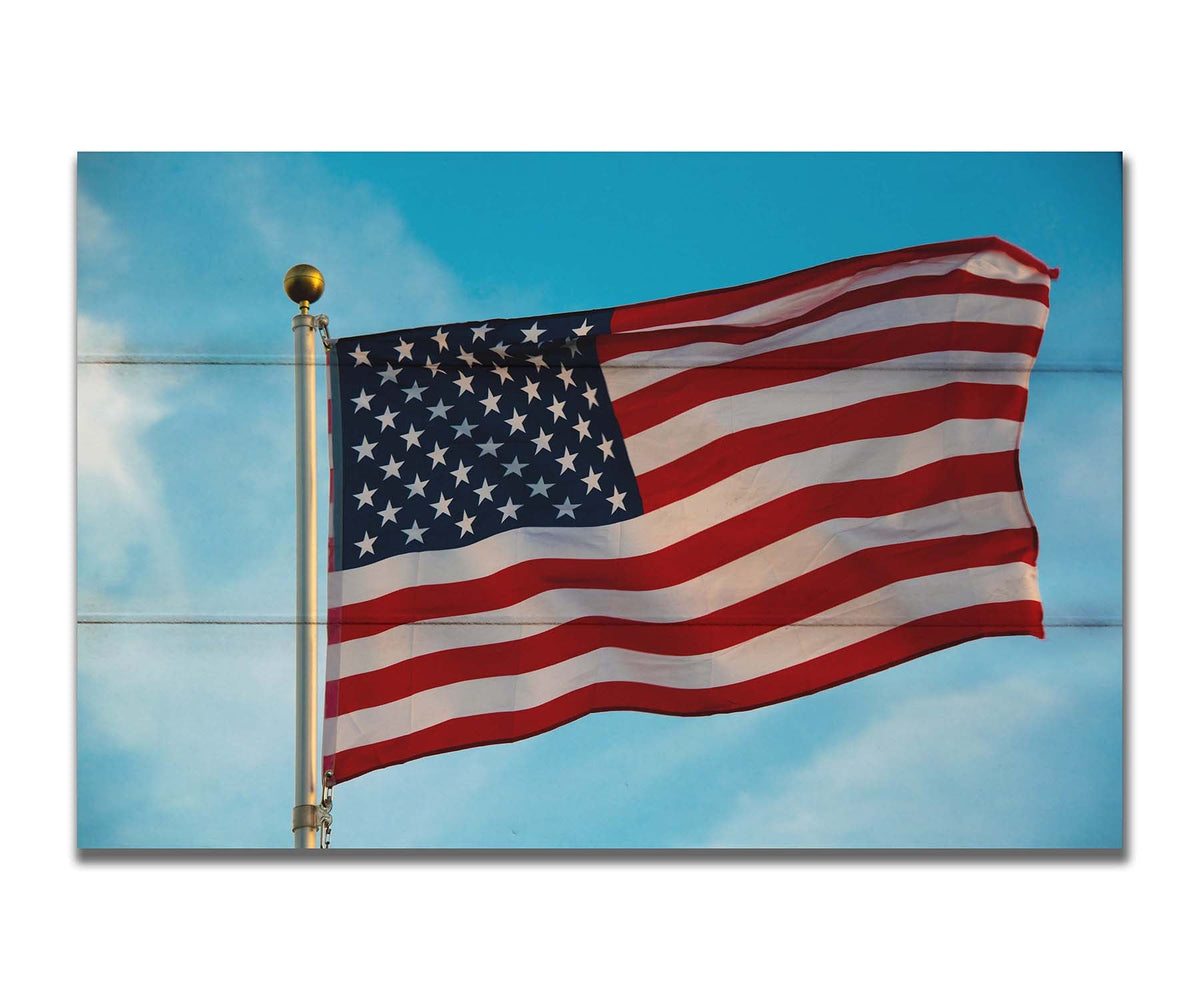 A photo of an American flag against a bright blue sky. Printed on a box board.