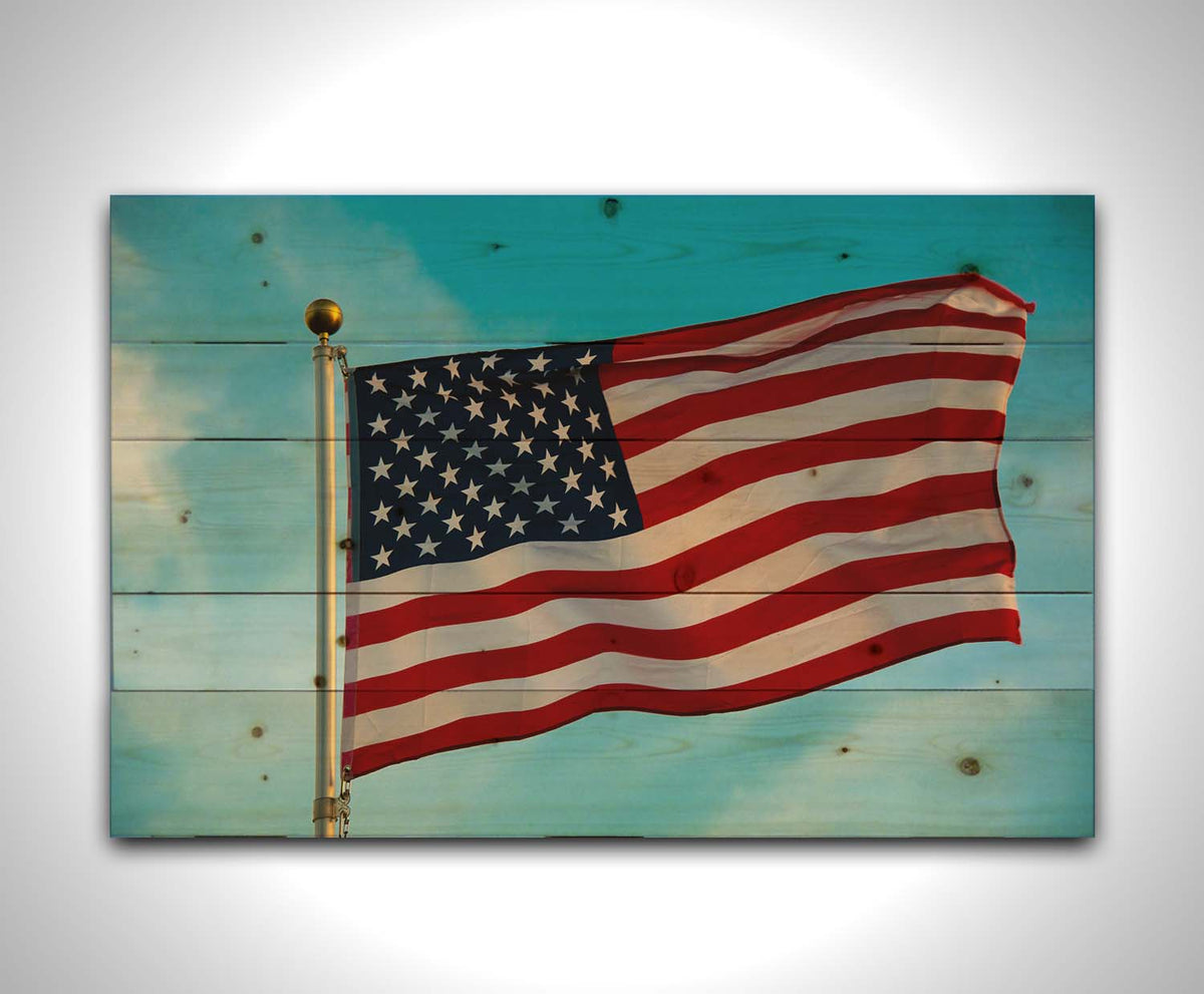 A photo of an American flag against a bright blue sky. Printed on a wood pallet.