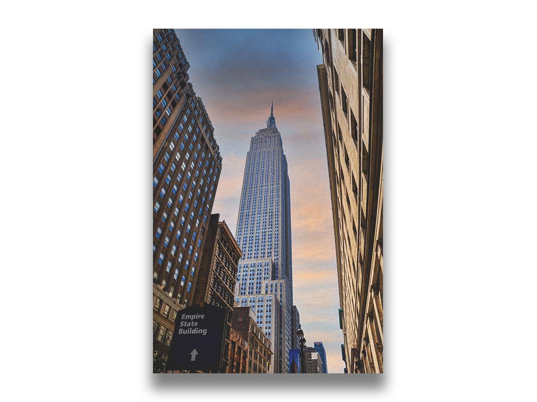 A photograph looking up at the Empire State Building in New York against a blue sky and orange clouds. Printed on canvas.