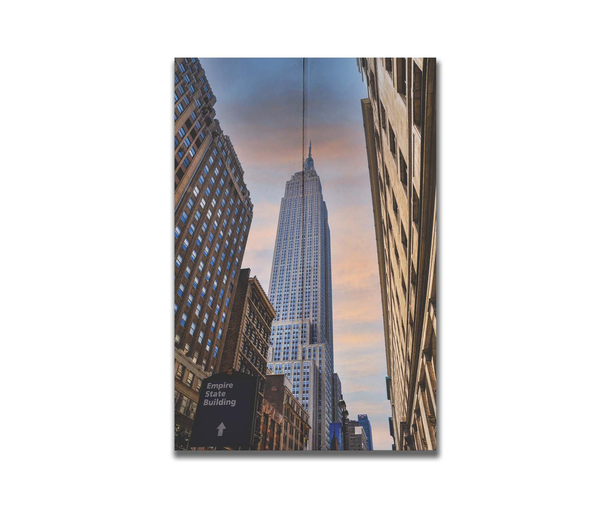 A photograph looking up at the Empire State Building in New York against a blue sky and orange clouds. Printed on a box board.