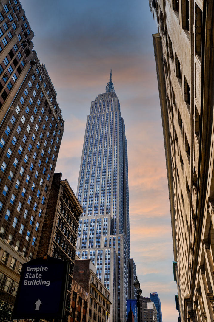 A photograph looking up at the Empire State Building in New York against a blue sky and orange clouds.