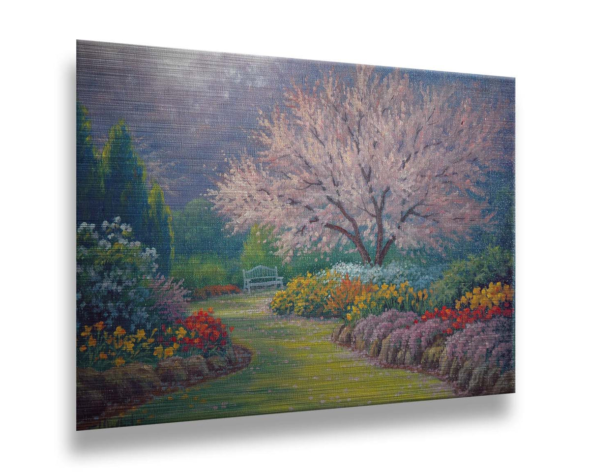 A painting of a grassy path through a garden, leading to a bench underneath a pink cherry blossom tree. A vast array of colorful flowers– such as red and yellow tulips, yellow daffodils, and lavender– line the path. Printed on metal.