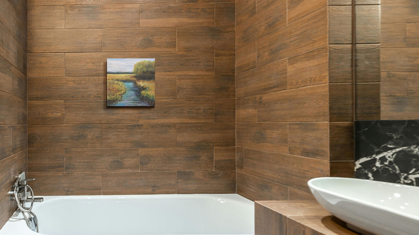 A painting hanging on a bathroom wall. A painting of a stream running through fields of yellow grasses, with clusters of trees to one side. Printed on a box board.