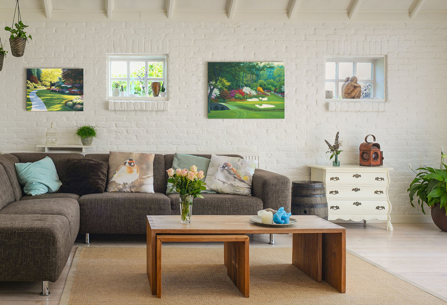A painting hanging on a living room wall. The first is a painting of a cobblestone path through a sunny, colorful, tidy garden. Printed on canvas. The second is a painting of the Augusta Nationals golf course in Georgia. The course is encircled by foliage and flowers of all colors, and a bridged stream runs through the center. A few golfers stand near a small sand pit, lining up a shot to the nearby hole. Printed on canvas.