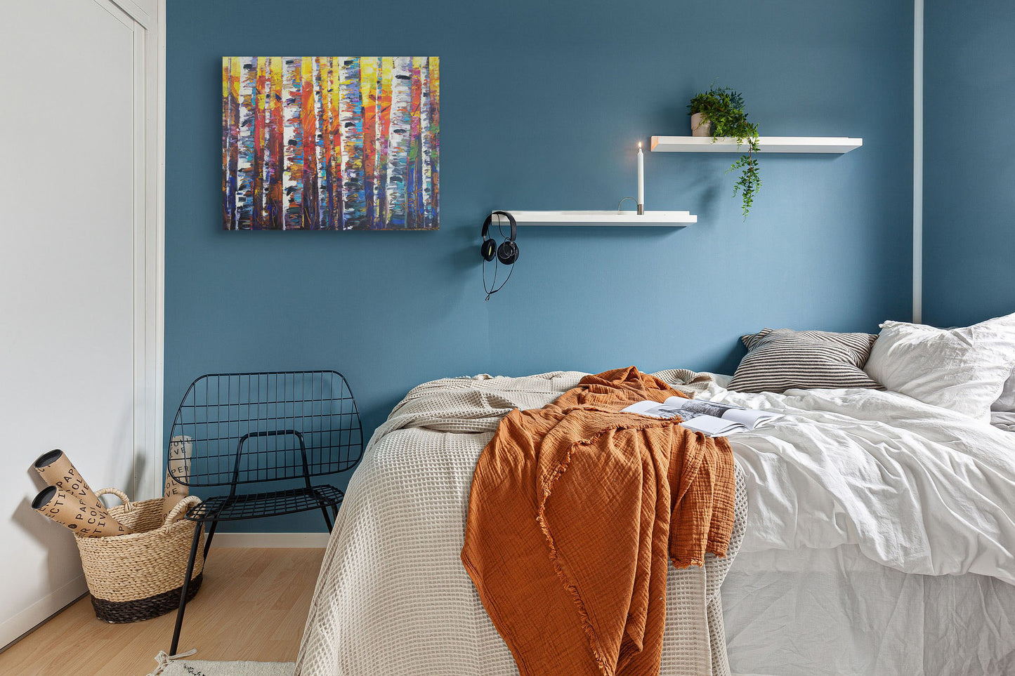 A painting hanging on a bedroom wall. A colorful painting of a forest of birch trees in arbitrary color, with white trunks against a yellow, red, and blue background made of large swaths of pallet knife paint. Printed on canvas.