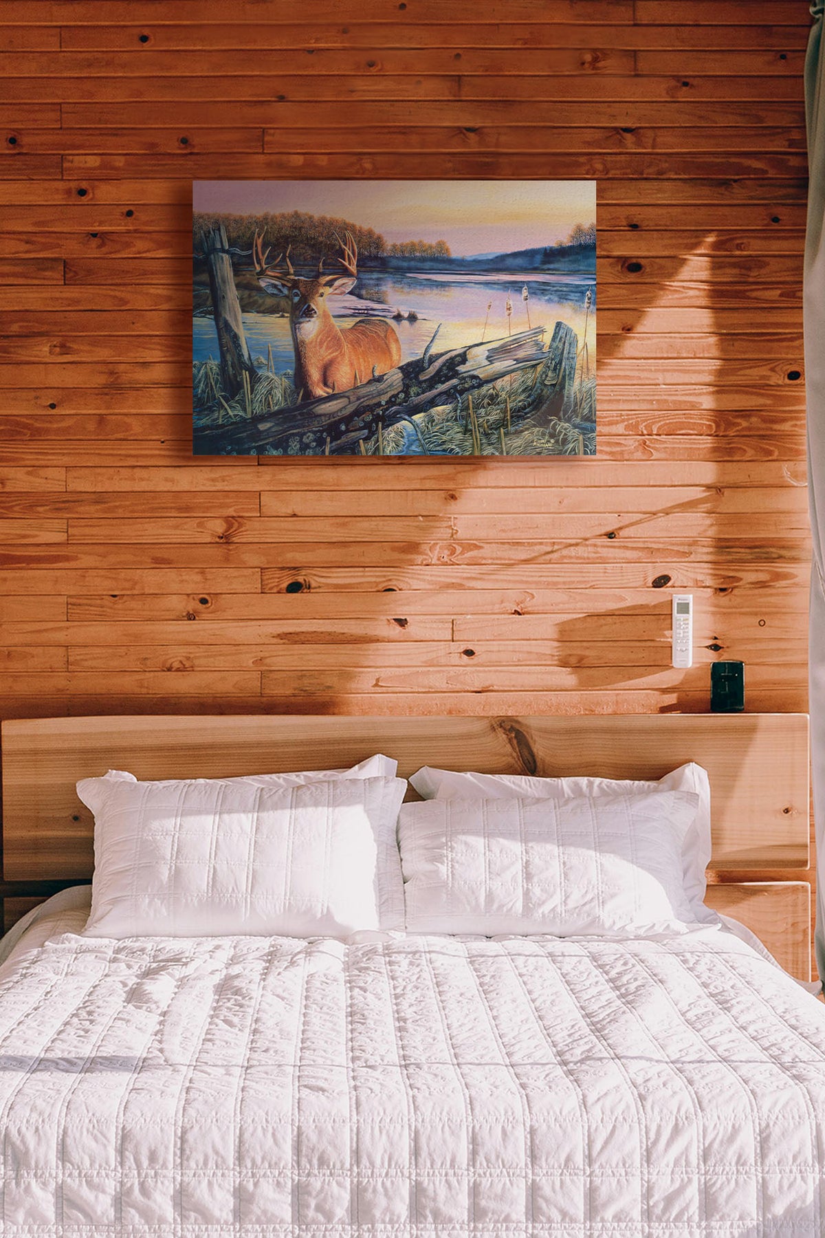 A painting hanging on a bedroom wall. Painting of a deer in front of a lake reflecting the morning sky. Printed on canvas.