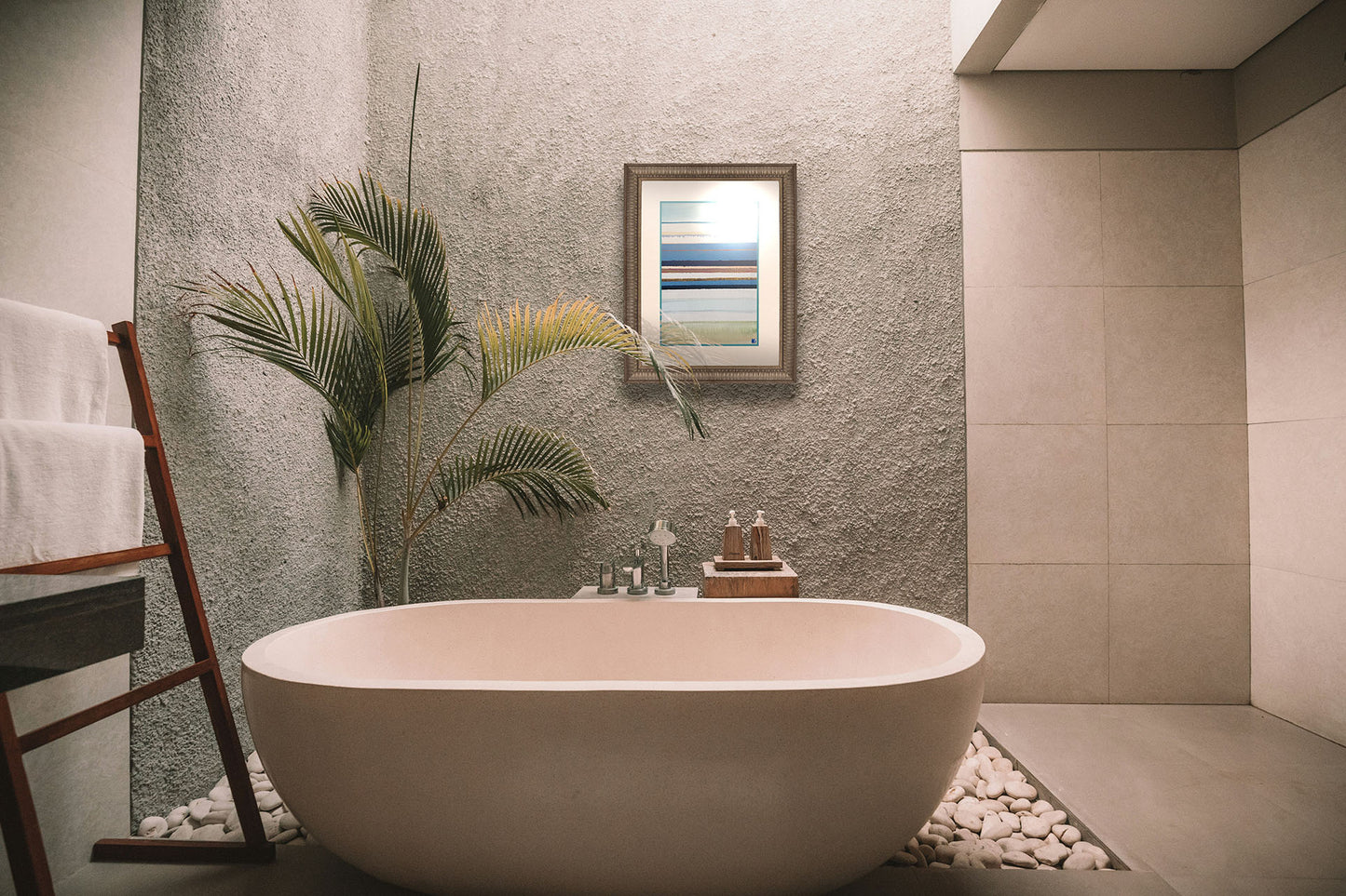 A painting hanging on a bathroom wall. An abstract painting arranging blue, white, yellow, and gold horizontal lines. The arrangement suggests the feeling of a shoreline. Printed on paper, matted, and framed.