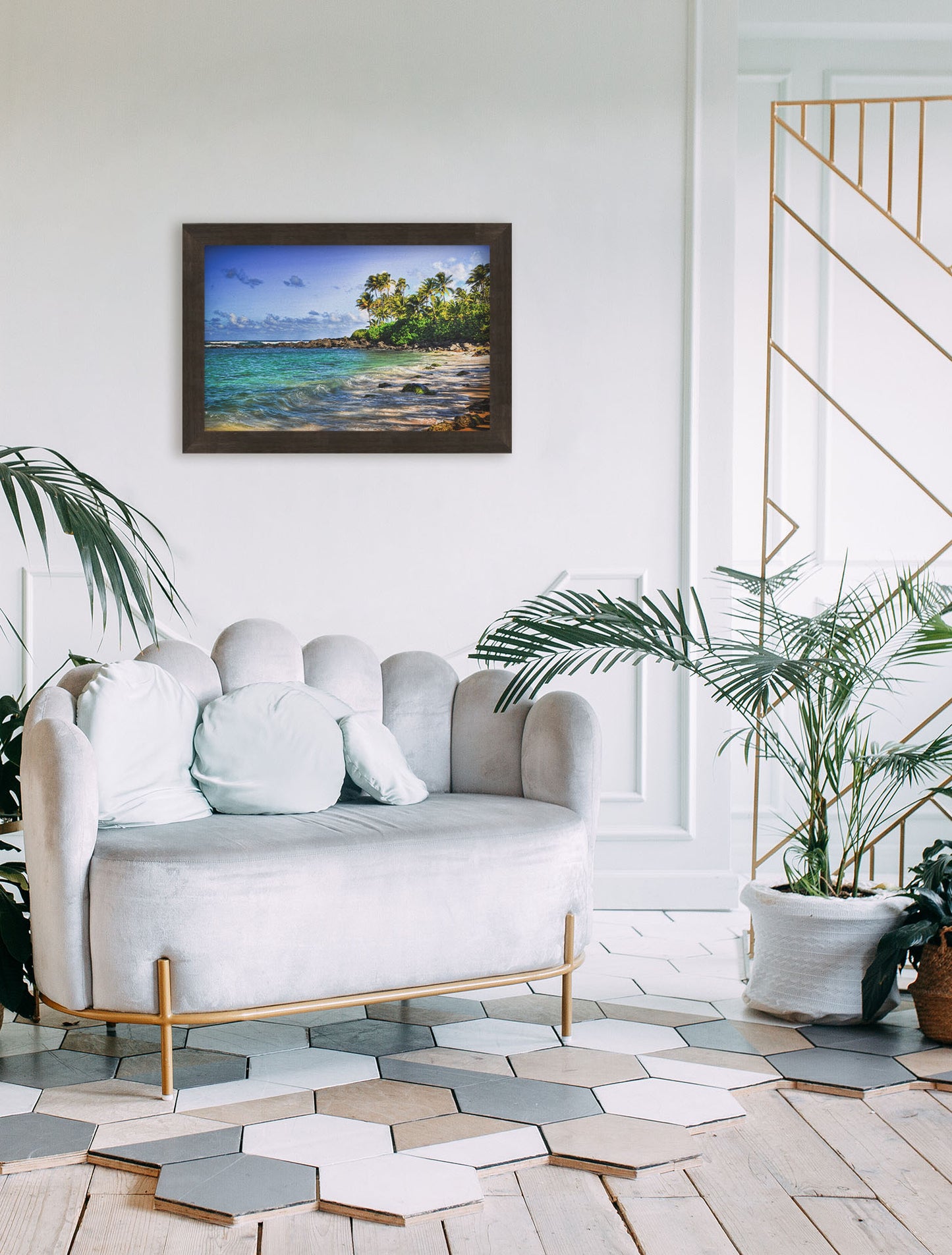 A photograph hanging on a wall. A photo of Laniākea beach. The water is a vibrant blue-green, and the stony beach circles around in the background where lush foliage and palm trees grow under a bright blue sky. Printed on canvas and framed.