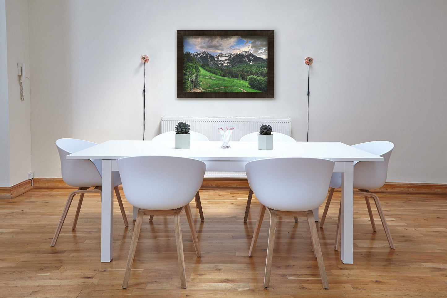 A photograph hanging on a dining room wall. Photo of snowcapped mountains and rolling green hills and forestry, at the Sundance Ski Resort in Utah. Printed on canvas and framed.