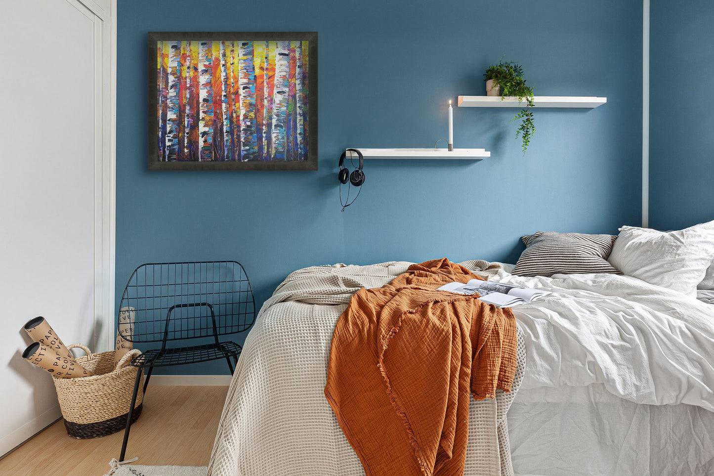 A painting hanging on a bedroom wall. A colorful painting of a forest of birch trees in arbitrary color, with white trunks against a yellow, red, and blue background made of large swaths of pallet knife paint. Printed on canvas and framed.