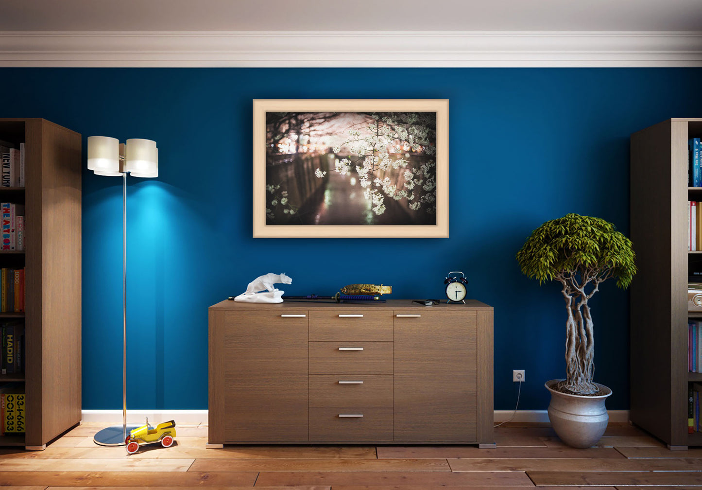 A photograph hanging on a study wall. A closeup photo of a branch of cherry blossoms, hanging over the Meguro River. Out of focus in the background, the river reflects twinkles of the city lights. Printed on canvas and framed.