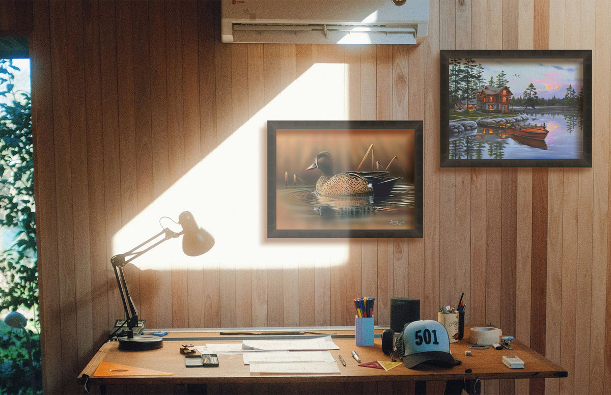 Two paintings hanging on a study wall. The first is a painting of a blue-winged teal waterfowl, swimming across the water past several brown reeds. Printed on canvas and framed. The second is a painting of a lakeside cabin, with a boat out on the water and geese overhead. Printed on canvas and framed.