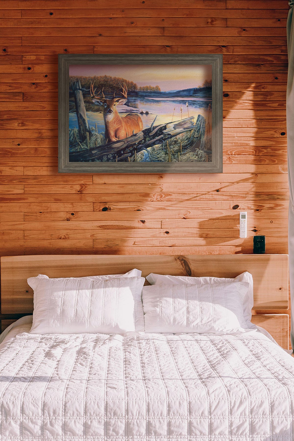 A painting hanging on a bedroom wall. Painting of a deer in front of a lake reflecting the morning sky. Printed on canvas and framed.