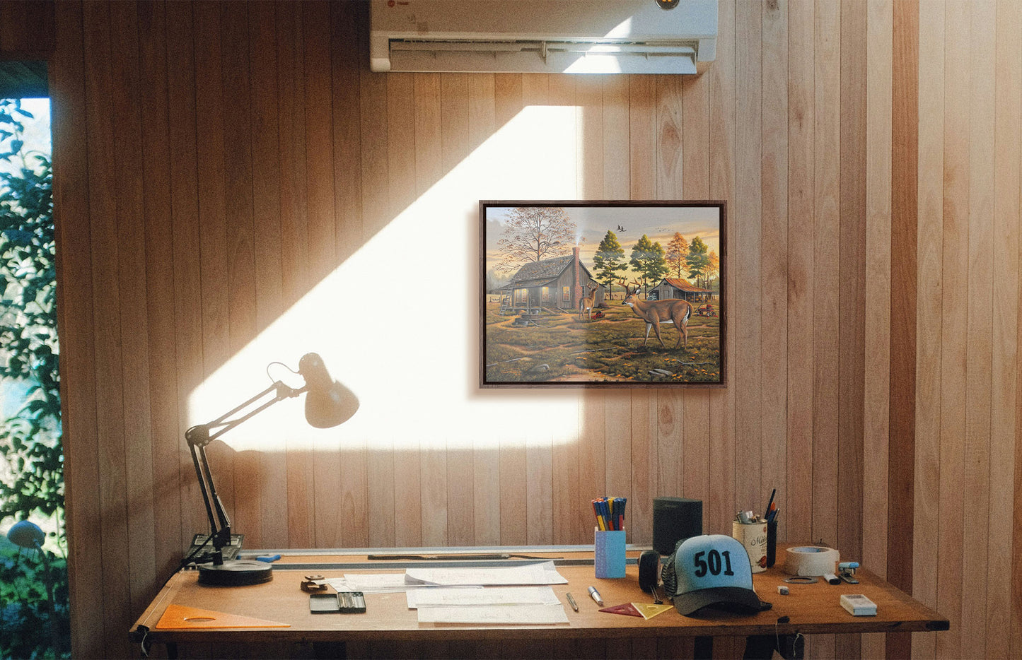 A painting hanging on a study wall. A painting of a farmhouse scene, featuring a fenced field, wood cabin, and an accompanying shed. In the foreground, deer are eating apples from wagons and baskets in the yard. Printed on canvas in a float frame.