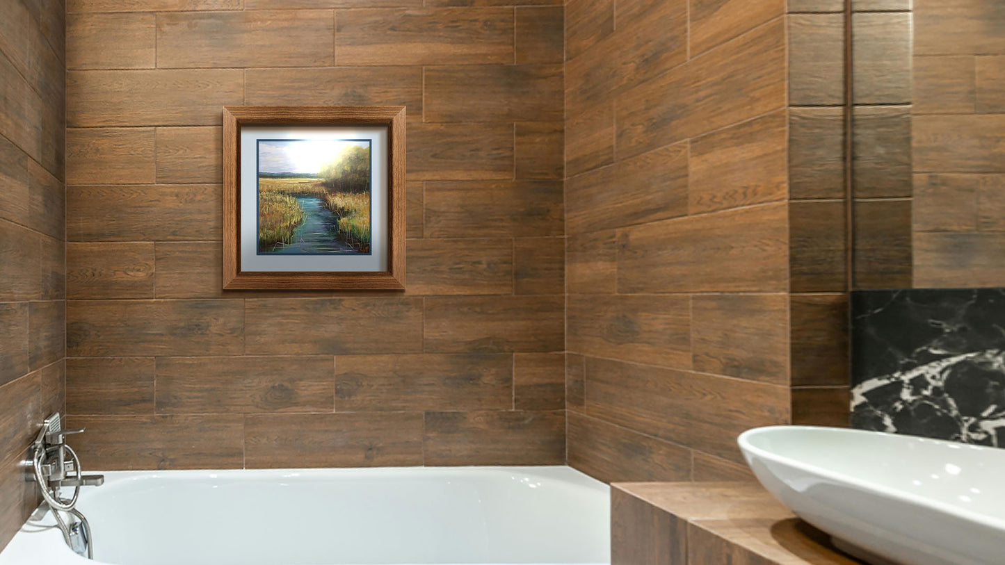 A painting hanging on a bathroom wall. A painting of a stream running through fields of yellow grasses, with clusters of trees to one side. Printed on paper, matted, and framed.