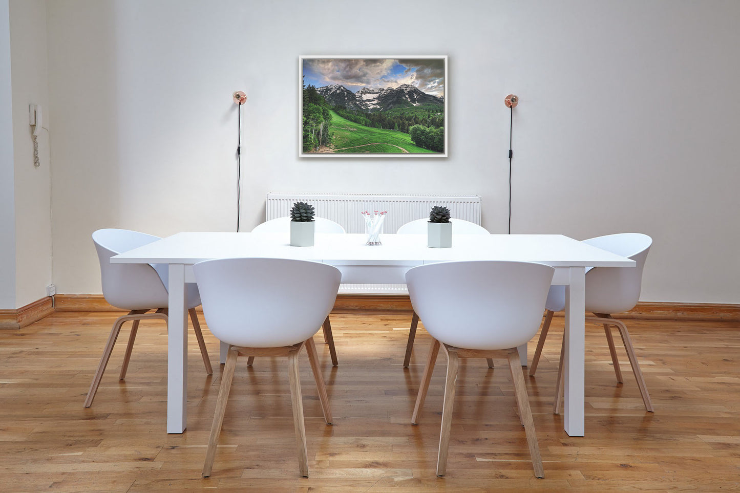 A photograph hanging on a dining room wall. Photo of snowcapped mountains and rolling green hills and forestry, at the Sundance Ski Resort in Utah. Printed on canvas in a float frame.