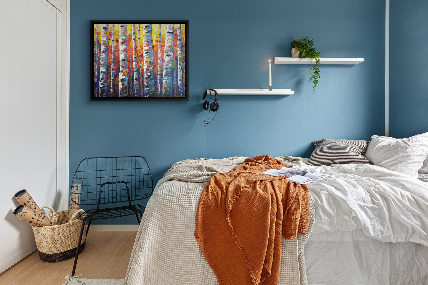 A painting hanging on a bedroom wall. A colorful painting of a forest of birch trees in arbitrary color, with white trunks against a yellow, red, and blue background made of large swaths of pallet knife paint. Printed on canvas in a float frame.