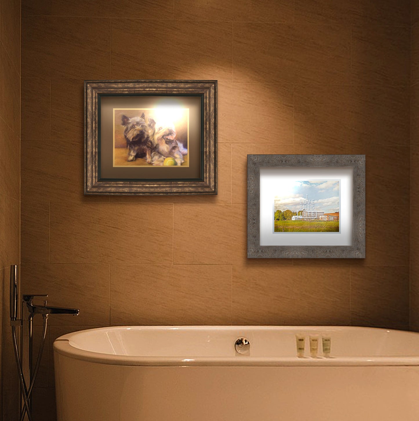 A painting and a photograph hanging on a bathroom wall. The first is a painting of two brown terrier dogs sitting with a tennis ball. Printed on paper, matted, and framed. The second is a photo of several barns, their associated pastures, and fields. The early signs of fall are present in the steadily changing leaves and crops. The sky above is wide, blue, and populated with fluffy clouds. It is overlaid with the phrase "I love this life." Printed on paper, matted, and framed.