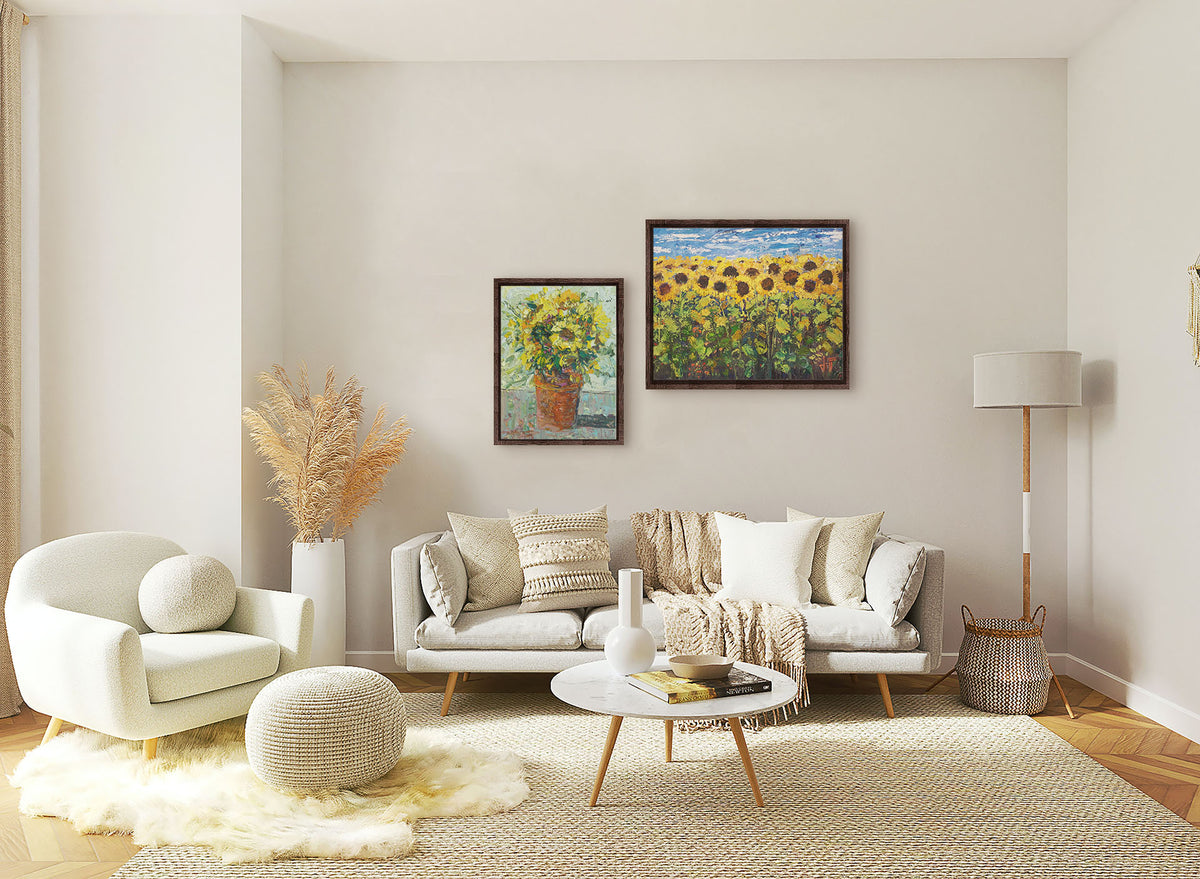 Two paintings hanging on a living room wall. The first is an expressive painting of an orange clay pot full of yellow sunflowers. Printed on canvas in a float frame. The second is an expressive painting of a yellow field of sunflowers against a bright blue sky. It is highly textured with visible brushstrokes and thick paint. Printed on canvas in a float frame.