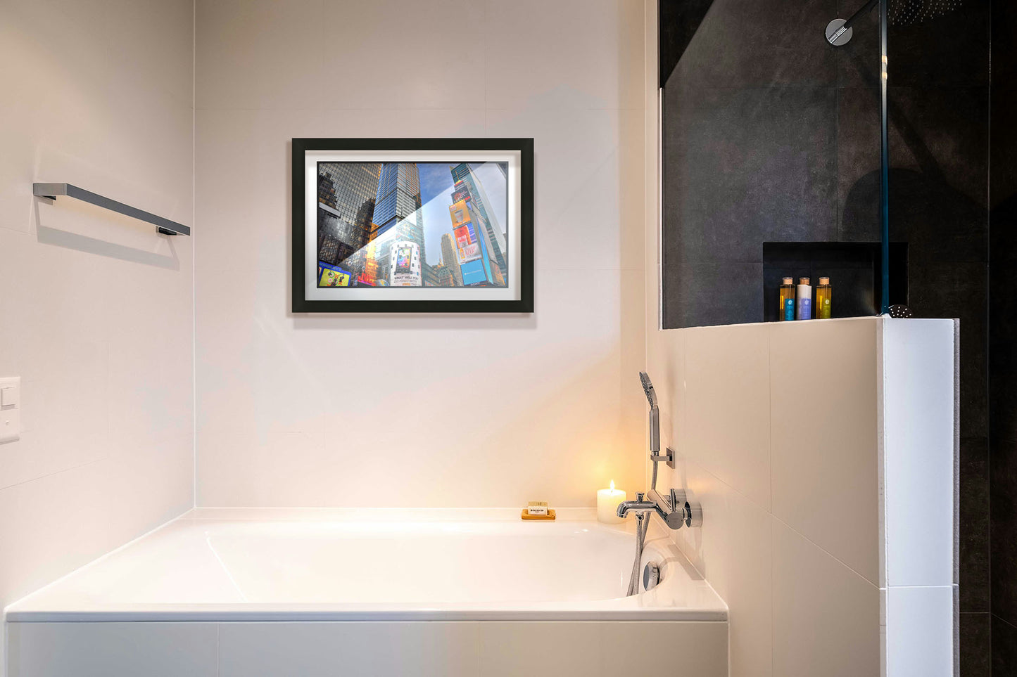 A photograph hanging on a bathroom wall. A photo looking up at the buildings and advertisements of Times Square in New York. Printed on paper, matted, and framed.