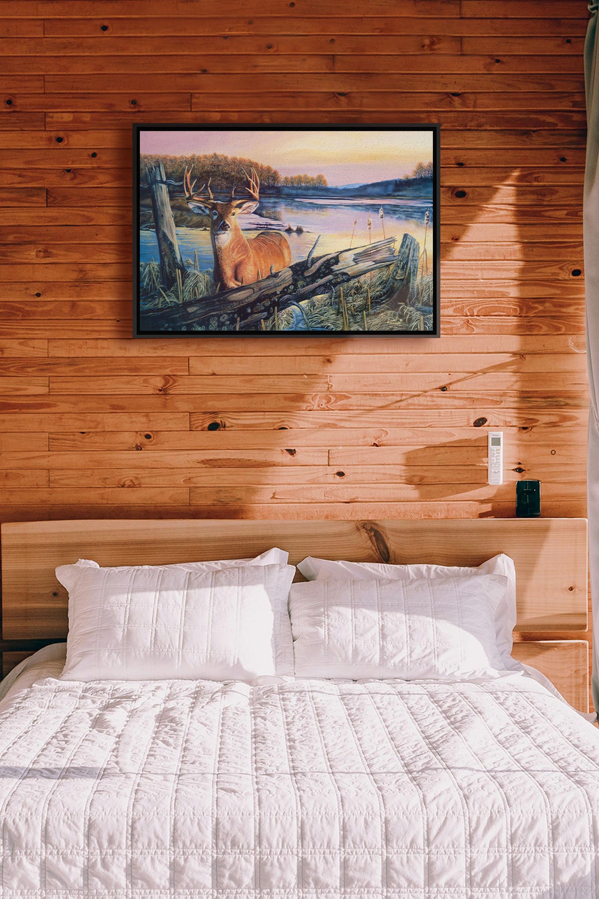 A painting hanging on a bedroom wall. Painting of a deer in front of a lake reflecting the morning sky. Printed on canvas in a float frame.