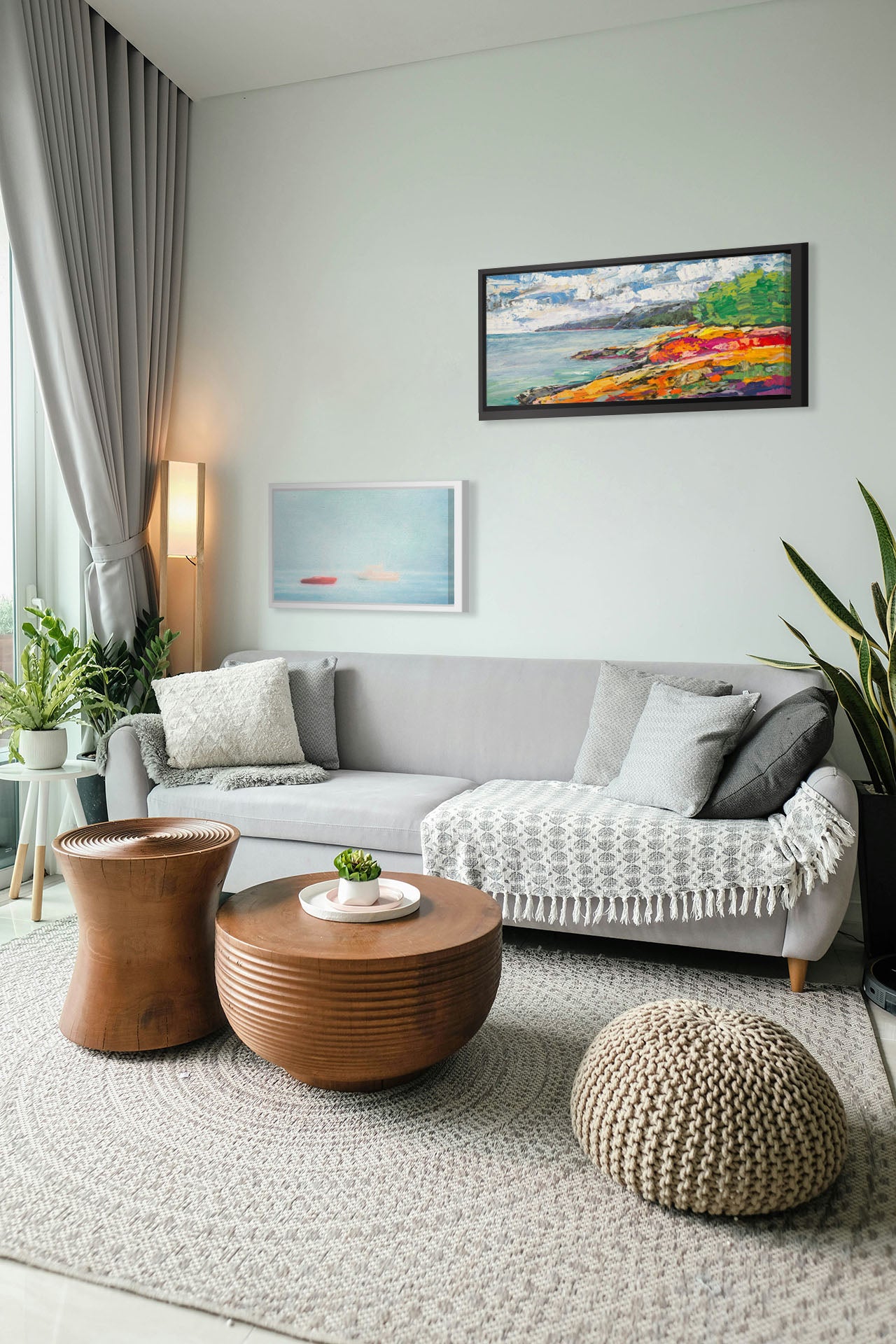 A photograph and a painting hanging on a living room wall. The first is a photo of a small red boat and a small white and yellow boat floating at sea. The photo is edited to have a soft, blurry quality which blends the sky and sea together on the horizon. Printed on canvas in a float frame. The second is a landscape painting of a beach. The smooth water, painted in local color, is contrasted by the brushstroke-textured beach, painted in arbitrary color. Printed on canvas in a float frame.