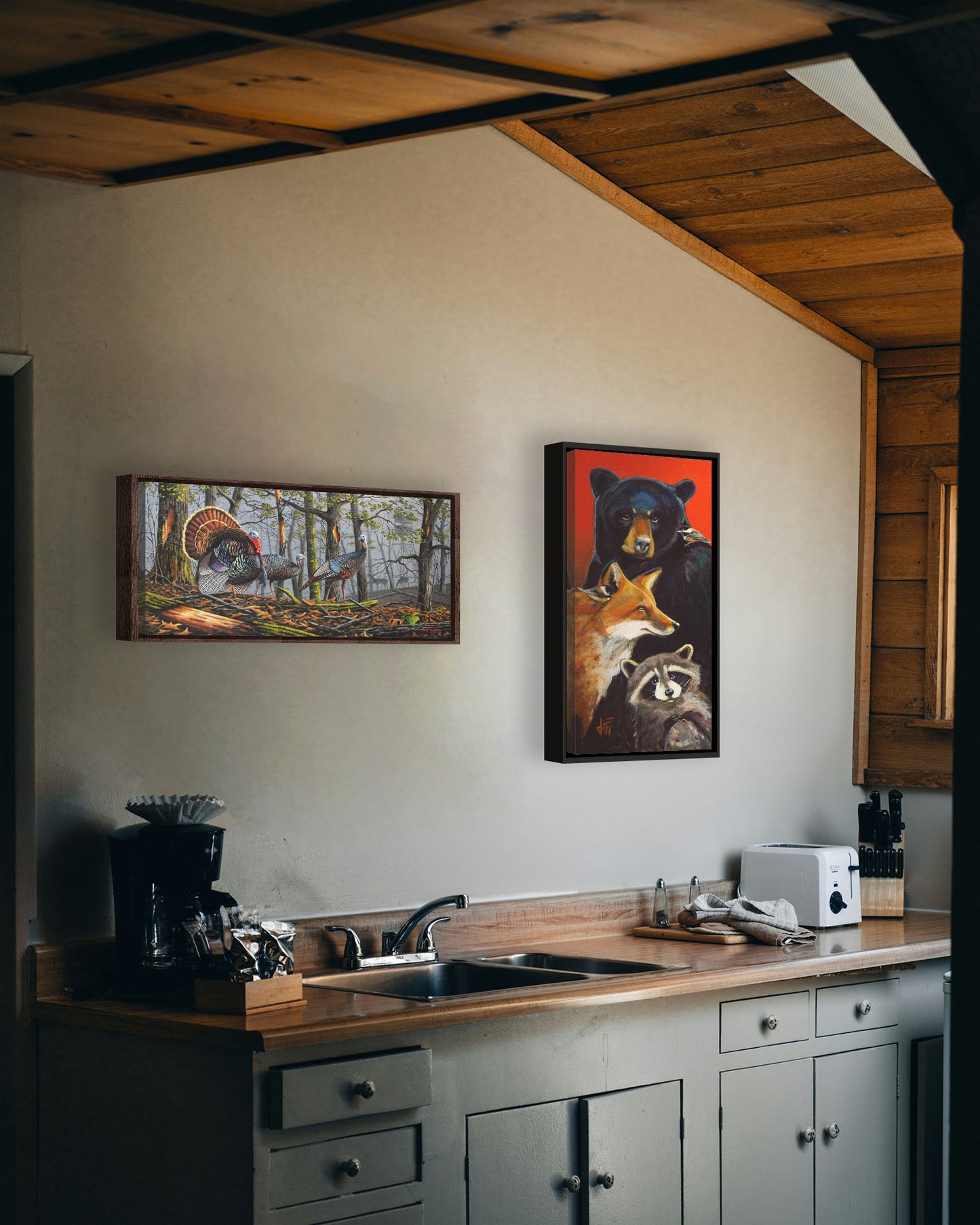 Two paintings hanging on a kitchen wall. The first is a painting of three turkeys walking through the woods on leaf-covered ground. In the distance, grazing deer and a hunting stand are visible through the fog. Printed on canvas in a float frame. The second is a painting collage of North American wildlife portraits. One black-capped chickadee perches on a black bear, and another perches on a red fox. A raccoon holds its paws together. Printed on canvas in a float frame.