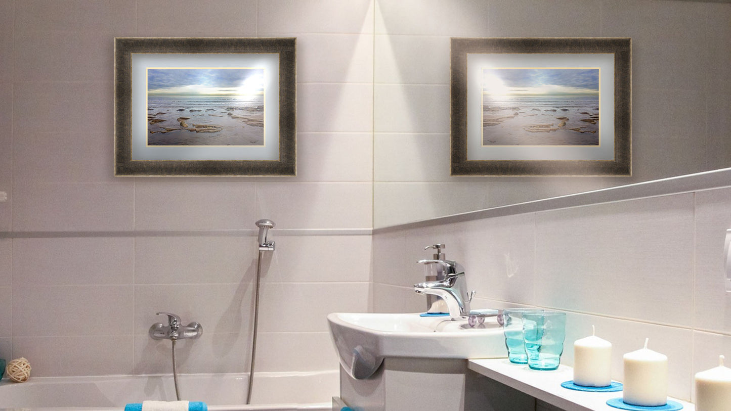 A photograph of the rocky shore of the North Sea at low tide. The sun peeks over the horizon through the partly cloudy sky. Printed on paper, matted, and framed.