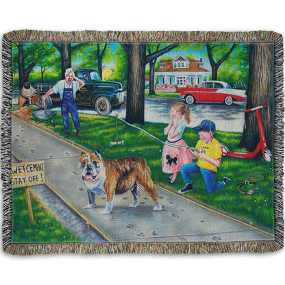 A woven throw blanket designed with a painting of a dog walking on wet cement, leaving paw prints everywhere. Two children are trying to catch the dog using a bone on a stick, and an onlooking construction worker panics. 