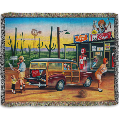 A woven throw blanket depicting a painting of a family lost on a road trip vacation. They have stopped at a small gas station in the desert to check their map for directions.