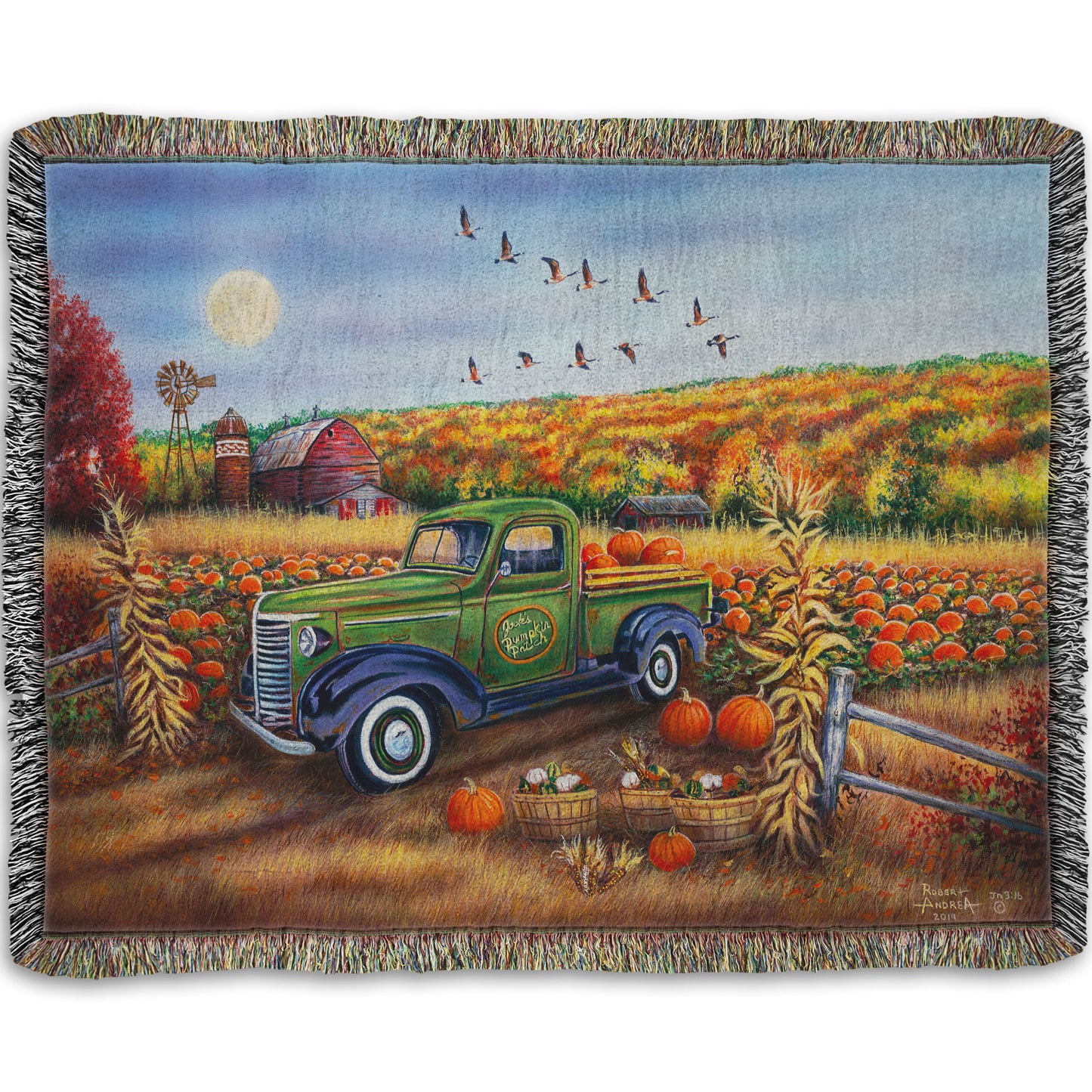 A woven throw blanket designed with a painting of a farm, featuring a field of pumpkins and a field of corn. There is a forest of yellow, orange, red, and green fall trees in the background, and geese fly overhead.