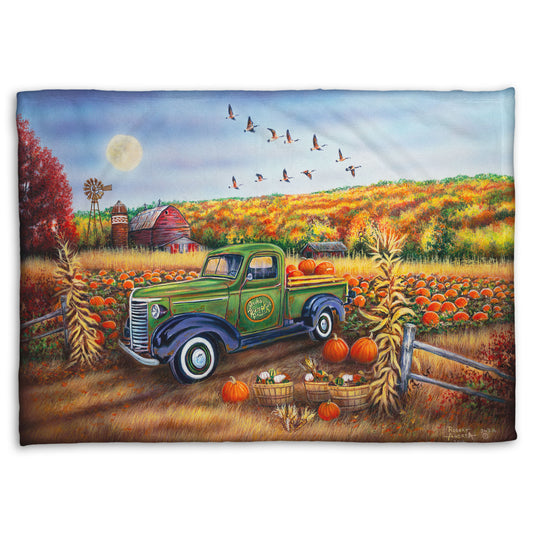 A coral fleece blanket designed with a painting of a farm, featuring a field of pumpkins and a field of corn. There is a forest of yellow, orange, red, and green fall trees in the background, and geese fly overhead.