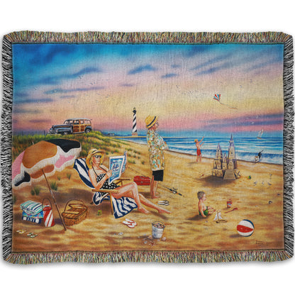 A woven throw blanket designed with a painting of a family vacationing on the beach. The adults relax while the children play, with one in the sand and another flying a kite with their dog.