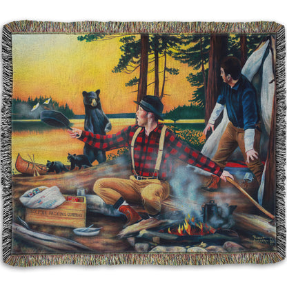 Woven throw blanket designed with a painting of two men camping and cooking a meal, looking back in shock at an approaching bear and her two cubs.