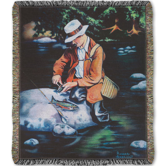 A woven throw blanket designed with a painting of a fisherman standing in the river, cleaning a fish he just caught.