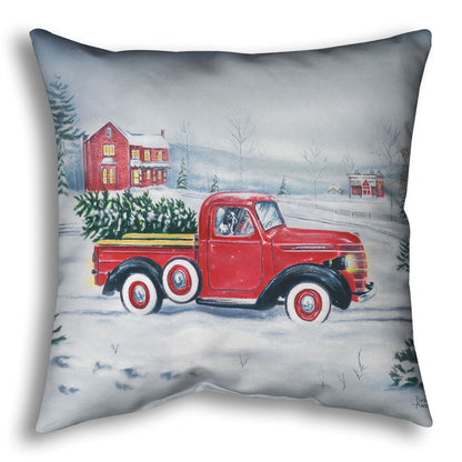 Decorative pillow printed with a red truck and Christmas tree driving through a snowy landscape.