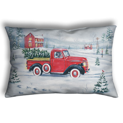 Decorative pillow printed with a red truck and Christmas tree driving through a snowy landscape.