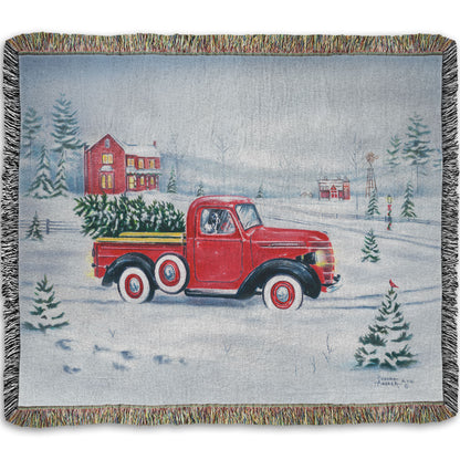 Woven blanket with a red truck and christmas tree design on a snowy background.